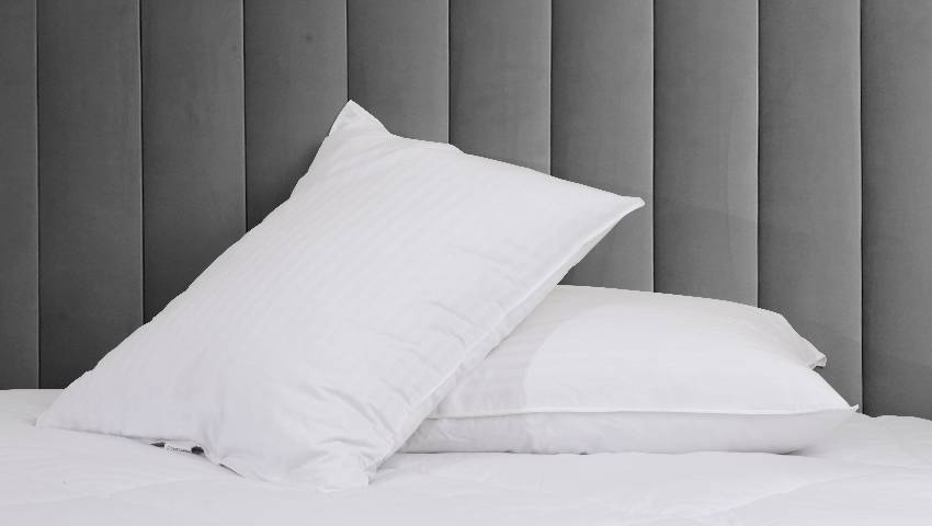 Dois Travesseiros em cima de uma cama com lenço branco e uma parede cinza